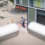 Ein Bauarbeiter kehrt vor der Wittenbacher Raiffeisenbank. Einen Tag nach dem Raubüberfall vom Montag hat der Alltag wieder Einzug gehalten. (Bild: Ralph Ribi)