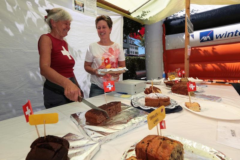An der 1. August-Feier in Beckenried. Wisi Imholz (links) übergibt Peter Mathis die Fischspezialität. nes Murer (links) und Heidi Scheuber verkaufen Kuchen. (Bild: Roger Zbinden / Neue NZ)