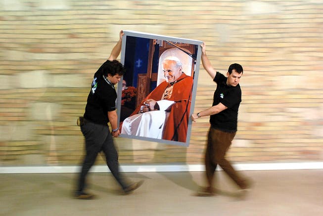 Zu viel Pomp? Mitarbeiter eines Museums hängen anlässlich einer Sonderausstellung über Johannes Paul II. ein Porträt des polnischen Papstes auf. (Bild: EPA)