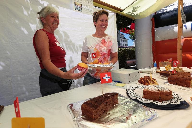 An der 1. August-Feier in Beckenried. Wisi Imholz (links) übergibt Peter Mathis die Fischspezialität. nes Murer (links) und Heidi Scheuber verkaufen Kuchen. (Bild: Roger Zbinden / Neue NZ)