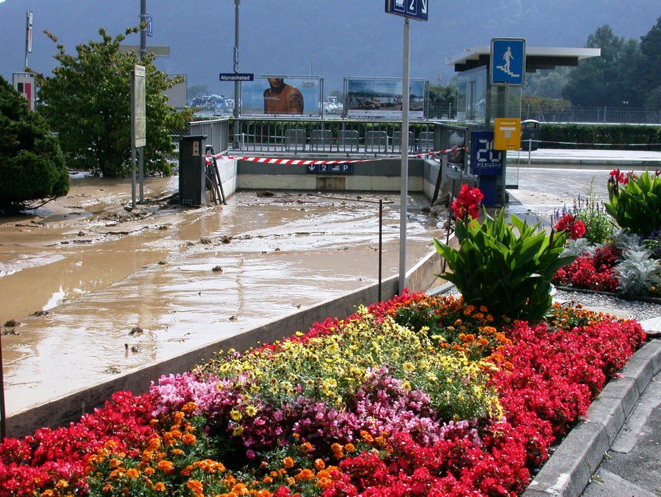 Kontraste in Alpnachstad: farbenprächtiges Blumenbeet und verschlammte Strassen und die überschwemmte Unterführung beim Bahnhof. (Bild: Archiv Neue OZ)