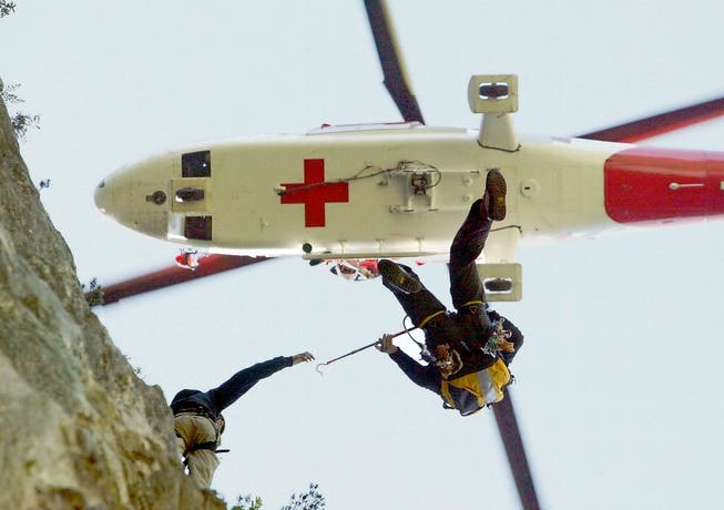 Ein Bergretter am Seil birgt einen verletzten Kletterer während einer Übung bei Schattdorf im Sommer 2005. Der Rega-Helikopter von der Einsatzbasis Erstfeld soll den Verletzten anschliessend ins Tal fliegen. (Bild: Keystone/Urs Flüeler)