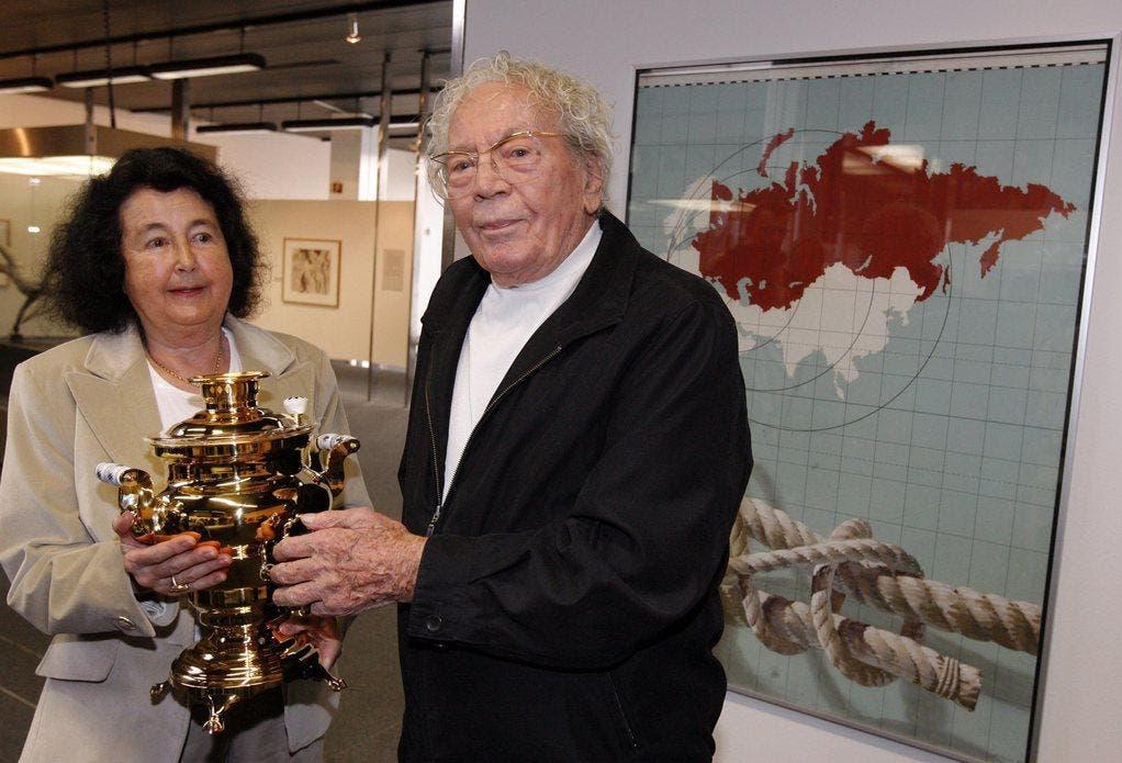 2010: Hans Erni und seine Frau Doris posieren mit dem Geschenk, einem russischen Samowar, vor dem im Jahr 1944 stark kritisierten politischen Plakat von Erni, nachdem dieser von der Gesellschaft Schweiz - Russland für seine Verdienste zur Völkerverständigung geehrt wurde. (Bild: Keystone)