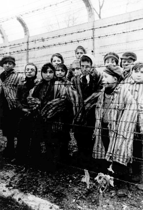 Eine Gruppe gefangener Kinder in Häftlingskleidung wartet am Tag der Befreiung von Auschwitz darauf, dass der Stacheldraht durchtrennt wird. (Bild: Keystone)