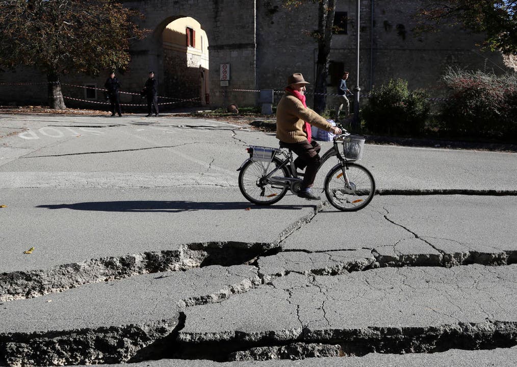 A man rides a bicycle past cracks in a road in Norcia, central Italy, after an earthquake with a preliminary magnitude of 6.6 struck central Italy, Sunday, Oct. 30, 2016. Central Italy was hit by another powerful earthquake Sunday, toppling buildings that had recently withstood other major quakes and sending panicked residents back into the streets, but causing no immediate loss of life. (AP Photo/Gregorio Borgia) (Bild: Keystone)