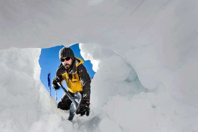 Ein alpiner Retter gräbt sich bei einer Übung mit einer Schaufel zu einem Verschütteten vor. (Bild: Keystone/Jean-Christophe Bott)