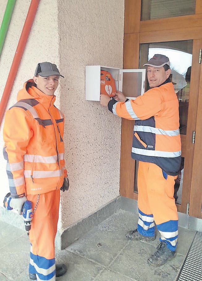 Bauamtsmitarbeiter der Gemeinde Jonschwil montieren die Defibrillatoren beim Schulhaus Notker. (Bild: pd)