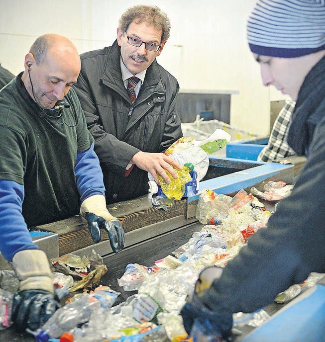 Regierungsrat Jakob Stark hält Plastikflaschen in der Hand, die aus dem PET-Recycling gefischt werden müssen. Am Sortierband der Müller Recycling AG in Frauenfeld arbeiten Carlo Machado (l.) und Igor Martin. (Bild: Reto Martin)
