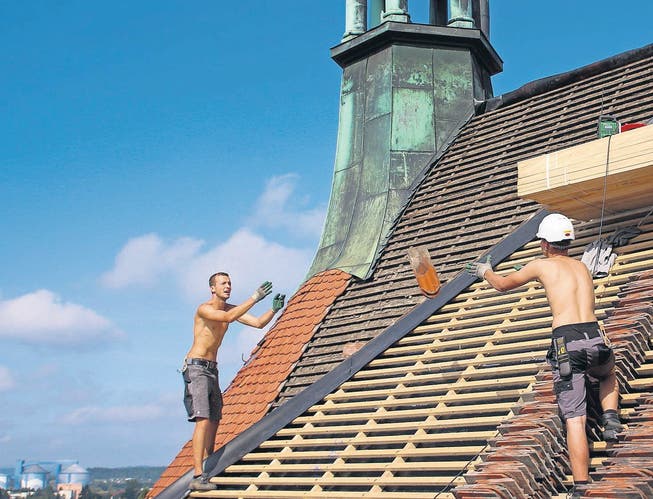 Die Dachdecker auf der katholischen Stadtkirche St. Nikolaus in Frauenfeld werfen einander die Ziegel zu. Das Dach wird neu eingedeckt. (Bild: Natalie Ammann)