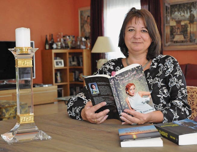 Schriftstellerin Sabine Ibing schmökert im Wohnzimmer durch ihre selbstgeschriebenen Bücher. (Bild: Amy Douglas)