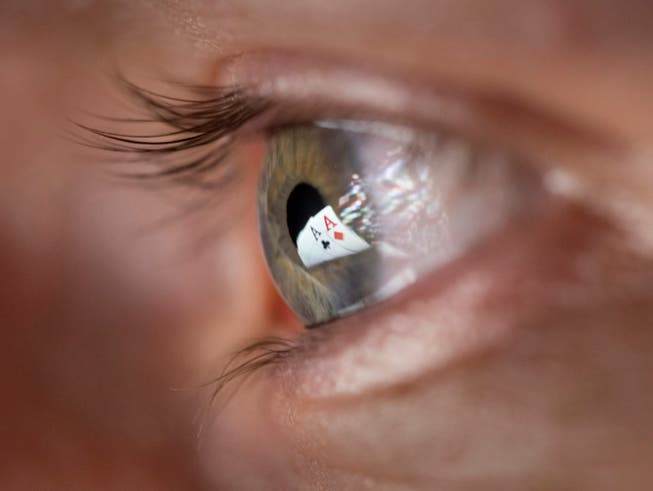 Zwei Ass-Spielkarten spiegeln sich in der Pupille eines Mannes, der Online-Poker spielt. Künftig dürfen auch Schweizer Casinos Online-Spiele anbieten. (Bild: Keystone/GAETAN BALLY)