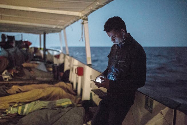 Ein Flüchtling überprüft auf einem Rettungsboot die Nachrichten auf seinem Smartphone. Bild: AP/Olmo Calvo (1. Juli 2018)