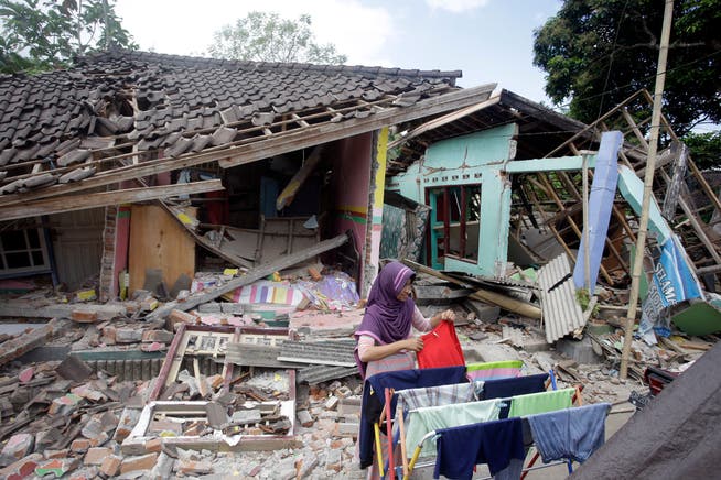 Eine Frau trocknet vor ihrem eingestürzten Haus ihre Wäsche. (AP Photo/Firdia Lisnawati)