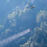 Ein Helikopter transportiert Löschwasser, um den Brandherd nach einem Kleinflugzeugabsturz am Lopper in Hergiswil im Kanton Nidwalden zu löschen. (Bild: Keystone/Urs Flüeler)