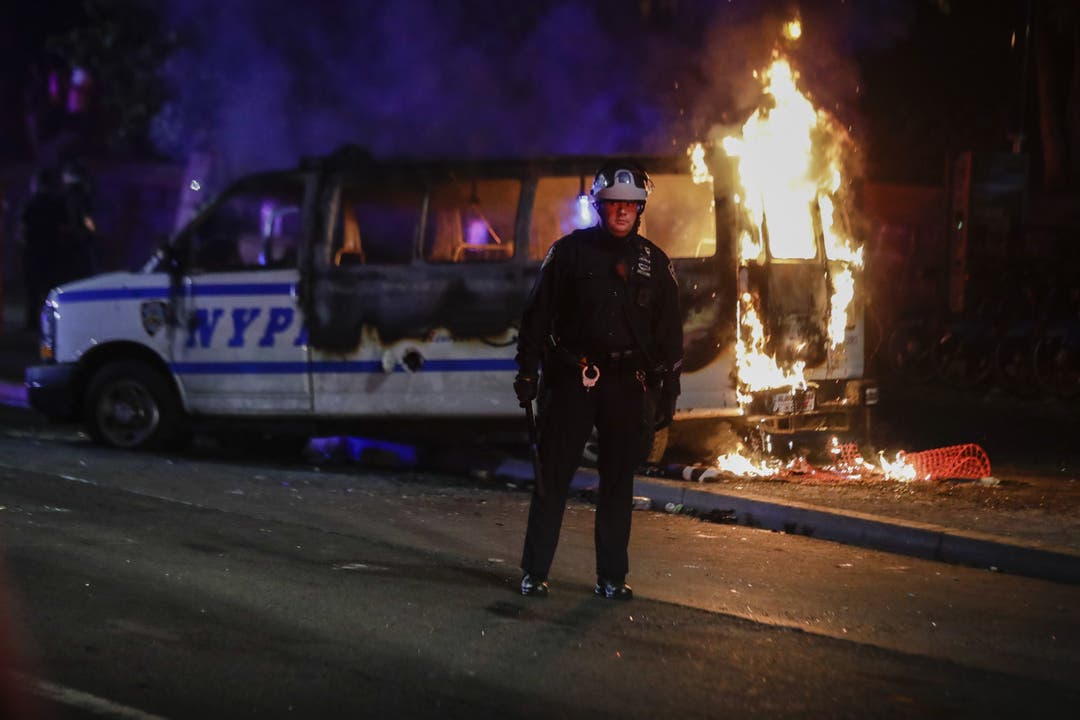 Ein Polizist beobachtet in Brooklyn, New York, die Menge, während hinter ihm ein Polizeiauto ausbrennt.