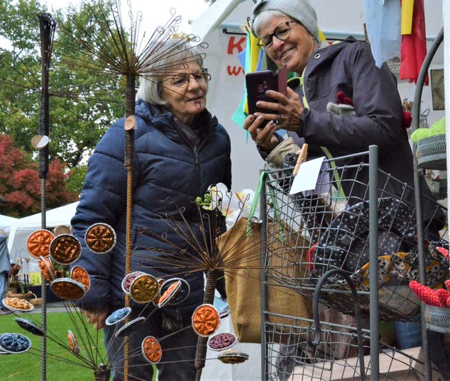 Zwei Besucherinnen halten am an einem Stand des Münchwiler Kunsthandwerksmarkts Eindrücke in Bildern fest.