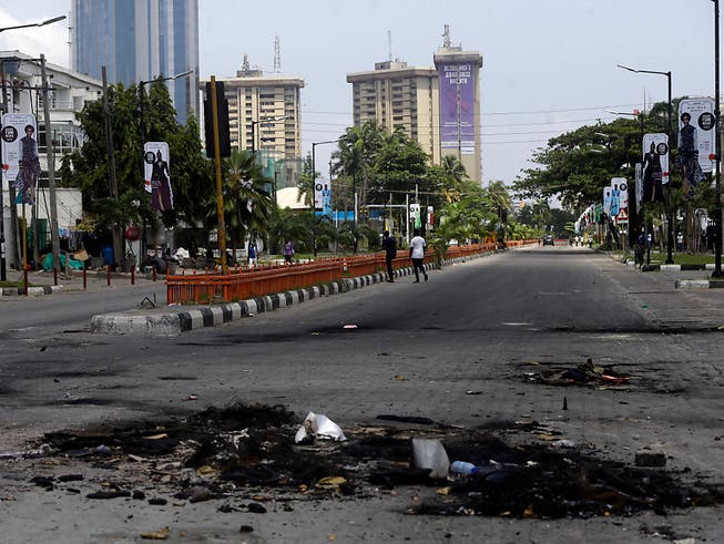 Auf einer sonst leeren Strasse liegen die Überreste von abgebrannten Strassenblockaden. Nach einem Blutbad bei einer Kundgebung gegen Polizeiübergriffe gehen die Proteste im westafrikanischen Nigeria unvermindert weiter. Foto: Sunday Alamba/AP/dpa