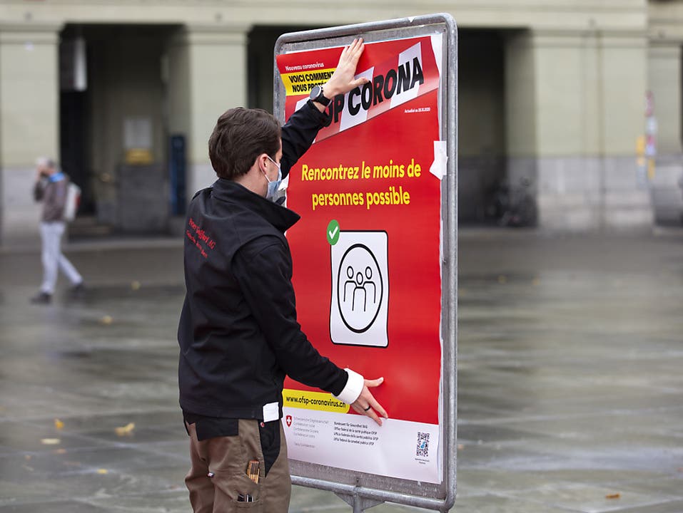 Coronavirus: Ein neues rotes BAG-Plakat mit der Verhaltensregel «Treffen Sie so wenige Menschen wie möglich"wird auf dem Bundesplatz in Bern installiert.