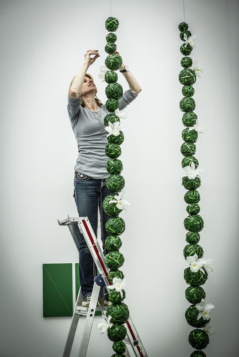 Priska Isenschmid hängt Kugeln aus Liliengras vor ein grün-weisses Werk von John Armleder.