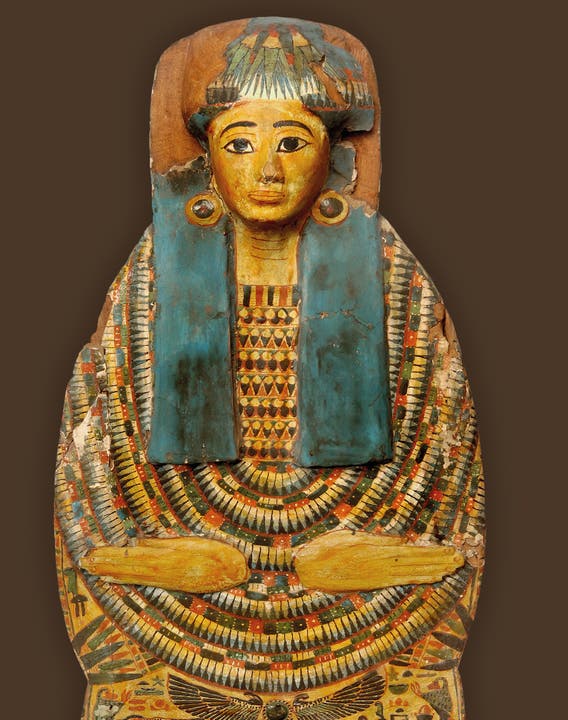 Mumienbrett der Dame Nes-Mut, deren vollständiges Sargensemble ausgestellt ist. Auf der Brust und um die Schultern ist ein farbenfroher Blumenschmuck dargestellt. Dritte Zwischenzeit, um 900 v. Chr. Leihgabe aus dem Ethnographischen Museum Neuchâtel.