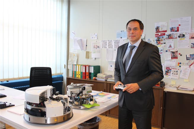 Direktor Michael Benker zeigt in seinem Büro zwei von Studenten konstruierte Roboter.