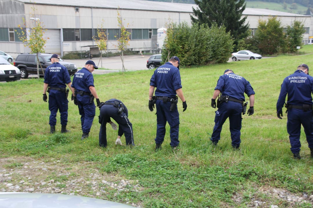  Polizisten suchen auf einer Wiese nach Spuren und der Tatwaffe.