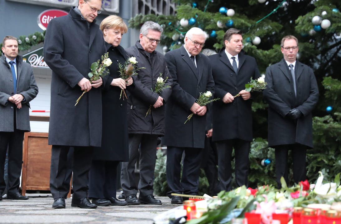 Bundeskanzlerin Angela Merkel legt am Berliner Weihnachtsmarkt Blumen nieder, neben ihr Innenminister Thomas de Maiziere (CDU), Aussenminister Frank-Walter Steinmeier (SPD) und Berlins Bürgermeister Michael Müller.