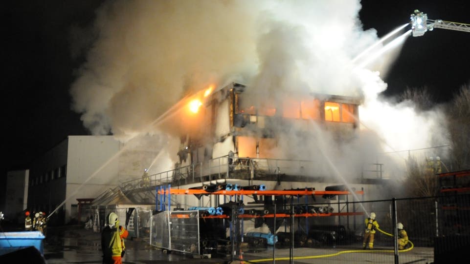 Von mehreren Positionen aus halten Feuerwehr-Einsatzkräfte am Abend des Grossbrandes Löschschläuche auf das Gebäude.