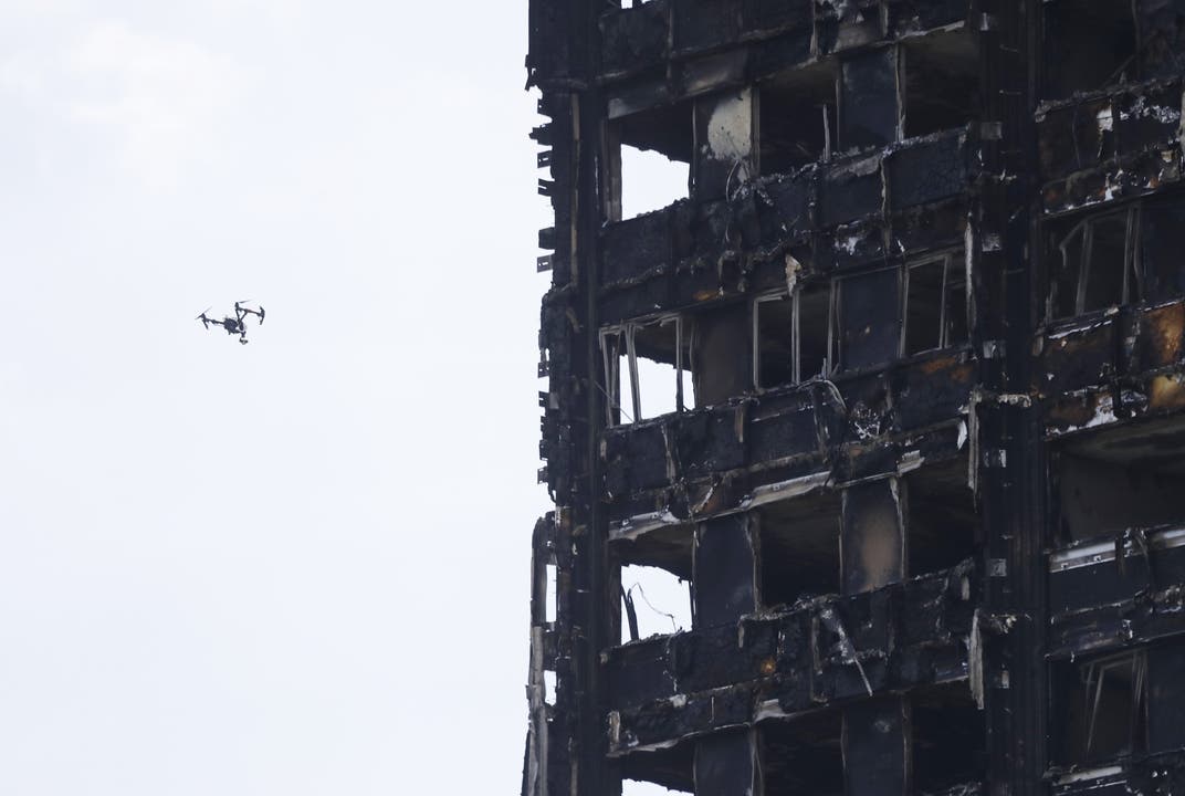Eine Drohne fliegt am niedergebrannten Hochhaus vorbei.