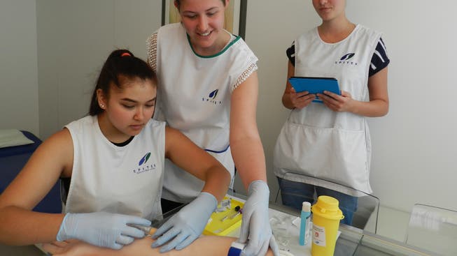 Deborah Müller (links) probt am Übungsarm eine Blutentnahme. Angela Jäggi und Jennifer Gamma beobachten sie dabei.