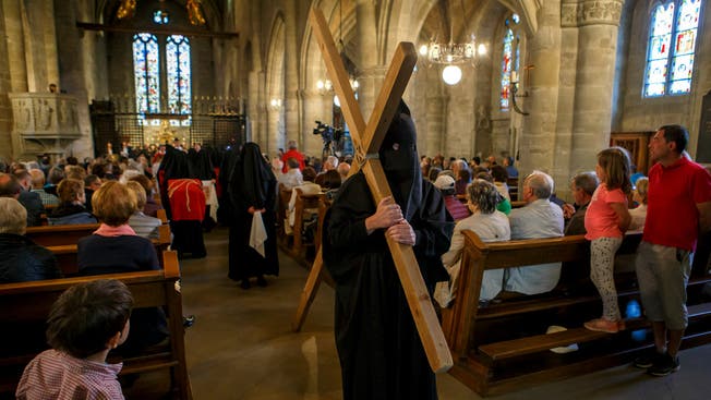 Eine verhüllte Frau trägt an der Karfreitagsprozession in Romont (FR) das Kreuz durch die Kirche.