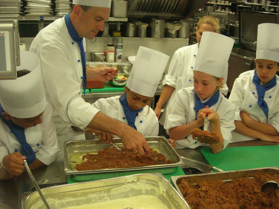  Küchen-Ausbildner Marco Breitenbach hilft beim Verteilen der Lasagne-Füllung.