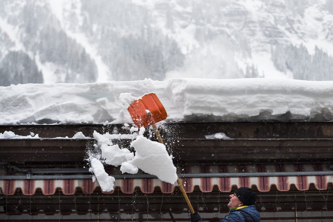 Ein Mann befreit ein Hausdach in Wengen im Berner Oberland von den Schneemassen.