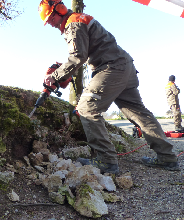 Zivilschützer arbeitet mit Spitzhammer, um ein Loch zu schaffen für die Eichenstelen.