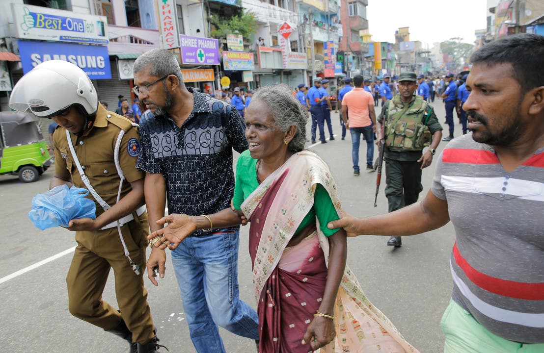 Männer helfen einer älteren Frau in der Nähe von einem der Explosionsorte in der Hauptstadt Colombo.