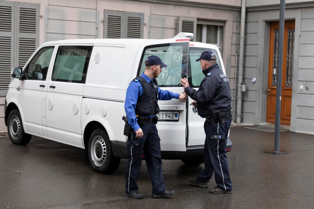 Zwei Polizisten öffnen die Tür des Wagens, in dem der Angeklagte zum Prozess gefahren wurde.