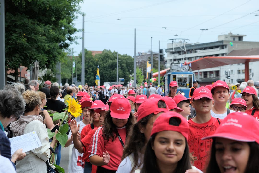 Rotes Kappenmeer: Viele Schülerinnen und Schüler nehmen am Umzug teil und klatschen freudig mit Zuschauern am Strassenrand ab.