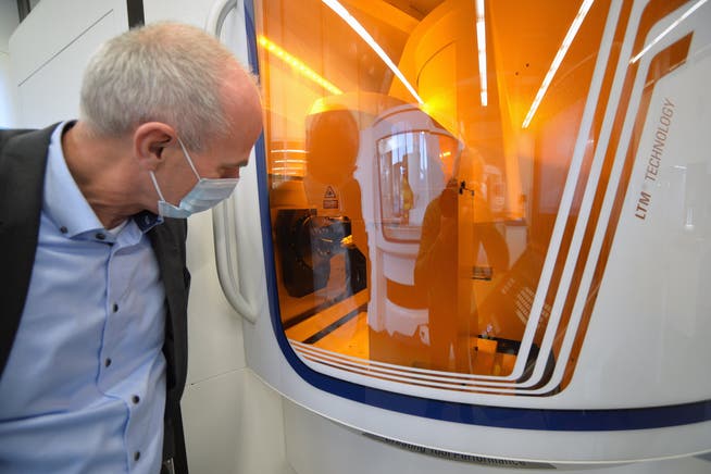 CEO Jürgen Schock betrachtet durch das orange Schutzglas eine Lasermaschine bei der Arbeit.