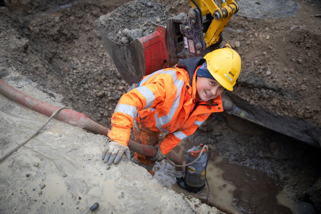 Eine Bauarbeiterin saugt Wasser aus dem Loch.