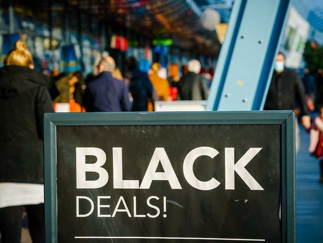 Passanten gehen vor einem Einkaufszentrum an einem Schild vorbei, das auf «Black Friday»-Angebote hinweist. Menschenmassen in Einkaufsstrassen und drohende Verstösse gegen Corona-Regeln: In den Niederlanden lehnen sich Städte gegen die Verkaufsaktion «Black Friday» auf. Foto: Marco De Swart/ANP/dpa