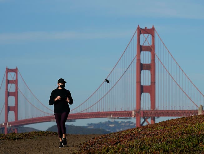 Eine Frau mit Mund-Nasen-Schutz läuft auf einem Weg vor der Golden Gate Bridge. Foto: Jeff Chiu/AP/dpa