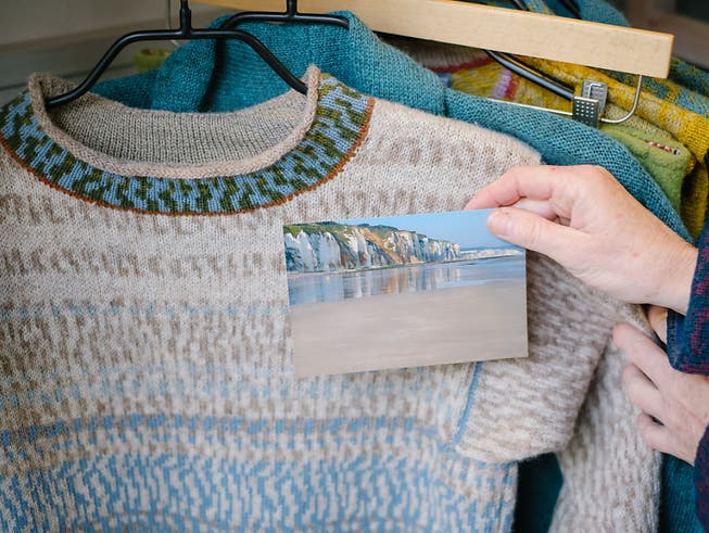 Die Textildesignerin Anne-Susanne Gueler hält in ihrem Werkstattladen «hand-werk» ein Foto aus der Normandie neben einen von ihr gestrickten Pullover. Gueler lässt sich häufig von Landschaften inspirieren. Foto: Ole Spata/dpa