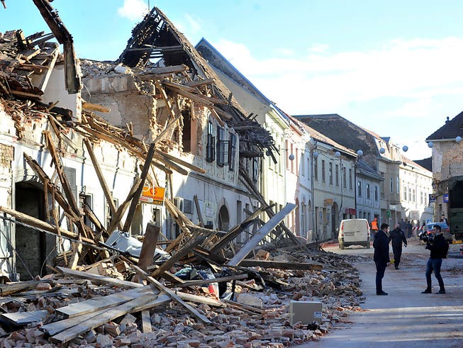 Zwei Passanten machen ein Foto vor den Trümmern eines durch ein Erdbeben eingestürzten Hauses. 