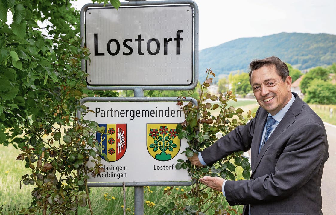 Thomas A. Müller, Gemeindepräsident von Lostorf, zeigt auf das rosenbestockte Partnerschaftsschild mit den beiden Gemeindewappen am Ortseingang. Die Partnerschaftsurkunde hängt in der Gemeindeverwaltung.