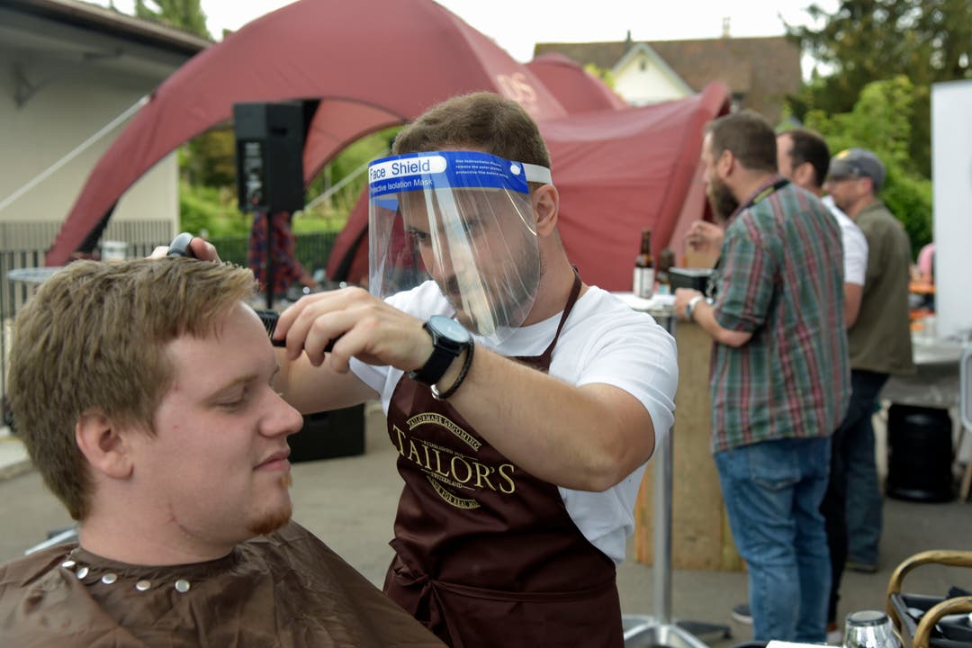 Barbier Jeton Miftari von «Toni's Barber Shop» legt draussen Hand an die Haare eines Kunden. Gut geschützt mit der Gesichtsmaske.