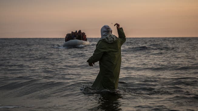 Ein Helfer winkt Neuankömmlingen auf einem Flüchtlingsboot an der griechischen Küste zu. 