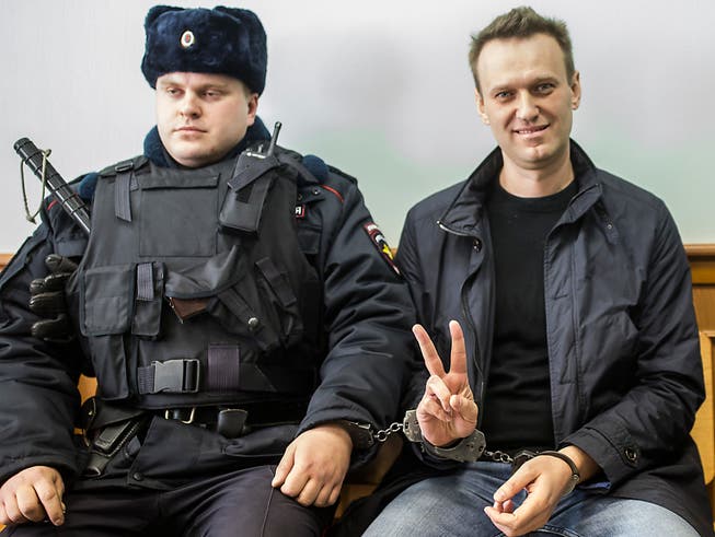ARCHIV - Alexej Nawalny (r) zeigt ein Victory-Zeichen, während er im März 2017 neben einem Sicherheitsbeamten im Gericht in Moskau sitzt. Foto: Evgeny Feldman/AP/dpa