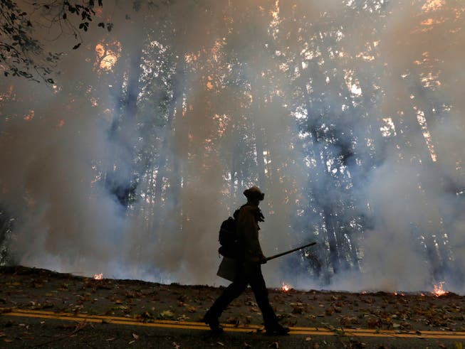 Ein Feuerwehrmann geht am Rande eines Gegenfeuers, welches die Brände in einem Waldgebiet unter Kontrolle bringen soll. Foto: Shmuel Thler/The Santa Cruz Sentinel/dpa
