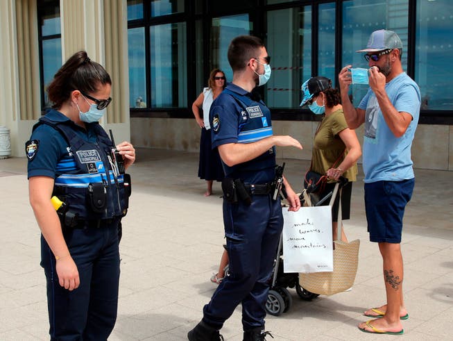 Polizeibeamte weisen Passanten auf das Tragen einer Mund-Nasen-Bedeckung hin. Im Kampf gegen Corona gilt in weiteren französischen Gemeinden jetzt eine Maskenpflicht im Freien. Foto: Bob Edme/AP/dpa