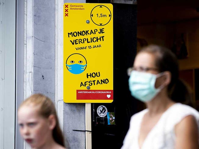 Eine Frau mit Mundschutz geht an einem Schild mit Informationen über die Maskenpflicht vorbei. Das Tragen eines Mund-Nasen-Schutzes aufgrund des Coronavirus ist an belebten Orten in Amsterdam Pflicht. Foto: sem Van Der Wal/ANP/dpa